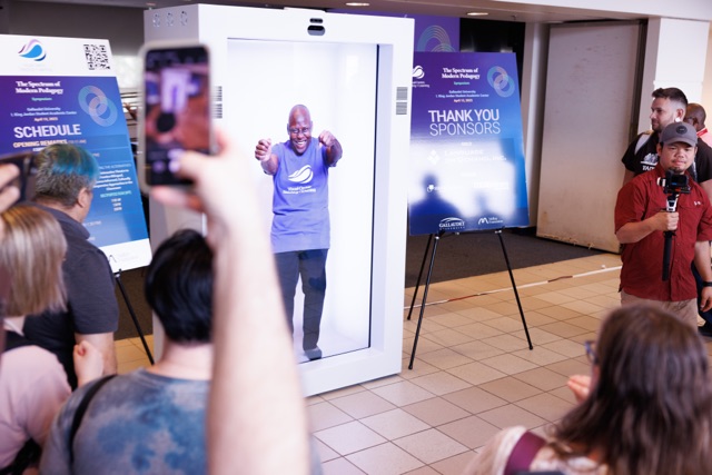 A group of participants in a hallway watching and videoing a hologram demonstration